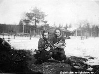 Kerpola(49)  Vasemmalla Kerpolan tytär Kyllikki Ahlgren (myöhemmin Rantanen, s. 6.12.1927) ja oikealla Kerpolassa evakkoina asuneen Ampujan perheen tytär Eeva istuvat ulkona, molemmilla nukke sylissään. Takana aitaa ja rakennus, mahdollisesti vanha navetta. Kyllikki on saanut Sointu Unelma -nimisen nukkensa lahjaksi kummeiltaan kauppiaspariskunta Kalle ja Tyyne Oksalalta.